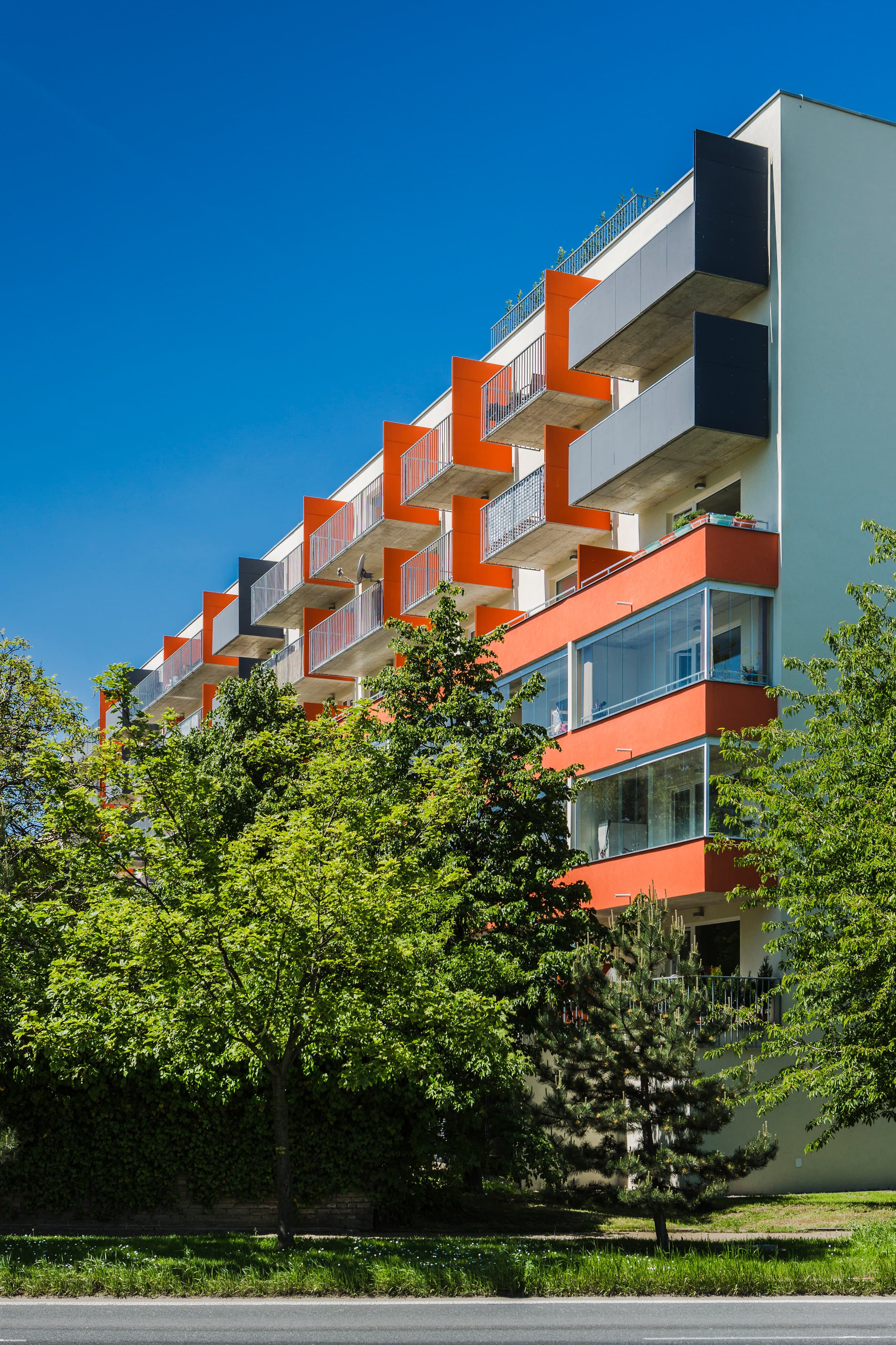 Boční pohled na bytový dům s prostřídanými oranžovými a bílými lodžiemi