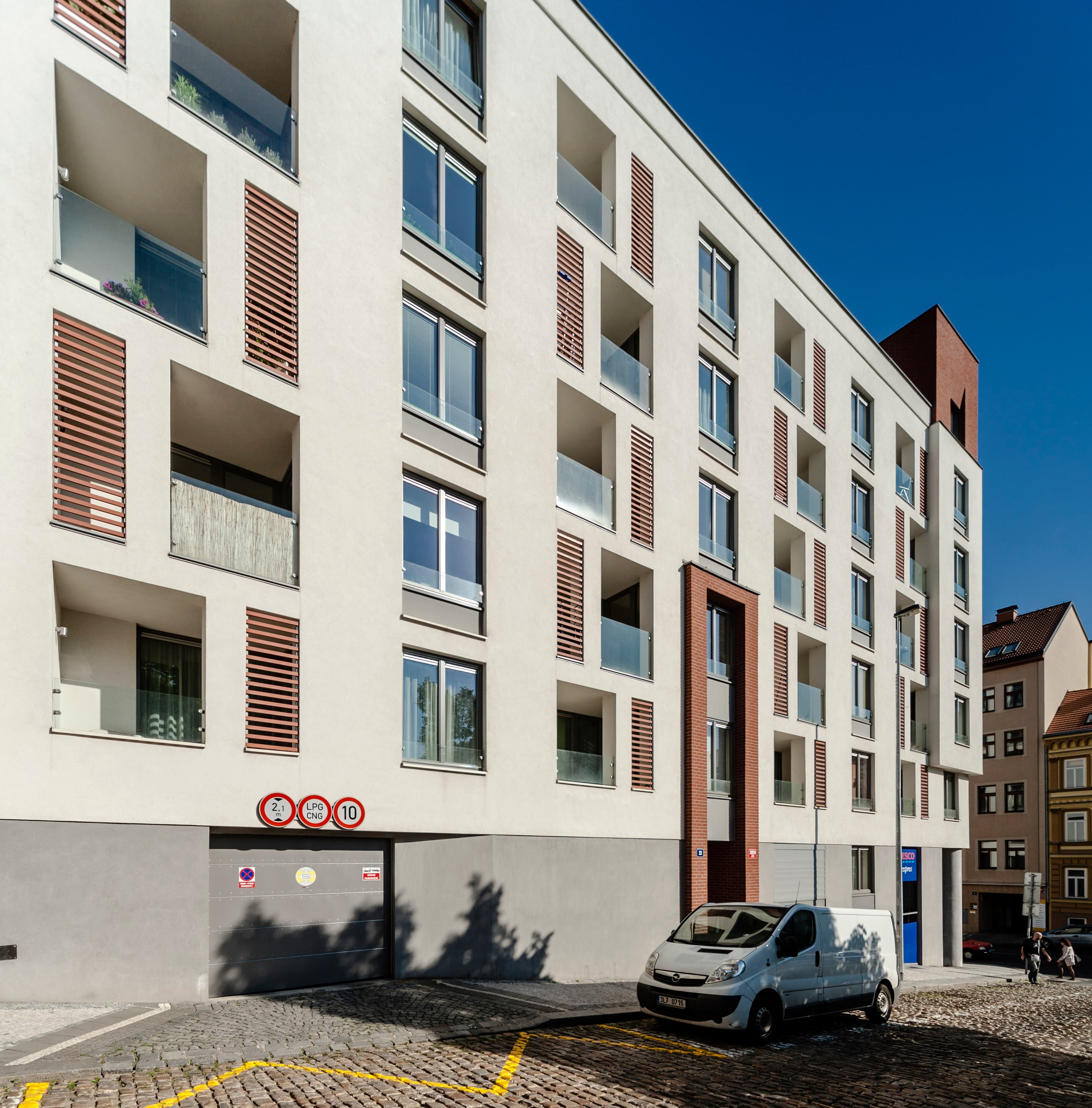 Fasáda do Prokopovy ulice s terakotovými stínicími křídly u lodžií, v parteru vrata do podzemních garáží