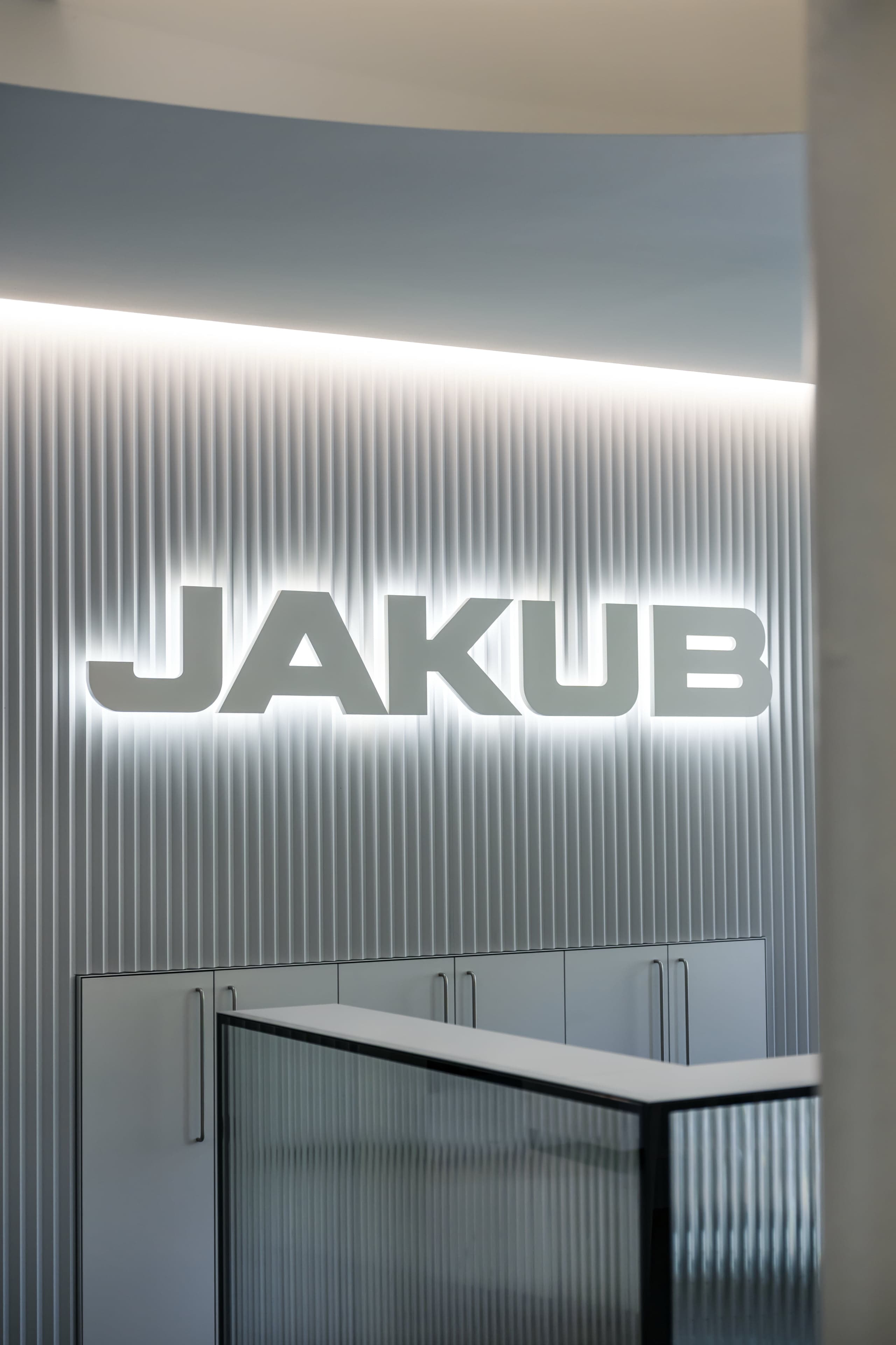 Detail podsvíceného loga JAKUB na stěně z vlnitého hliníkového plechu Prefa