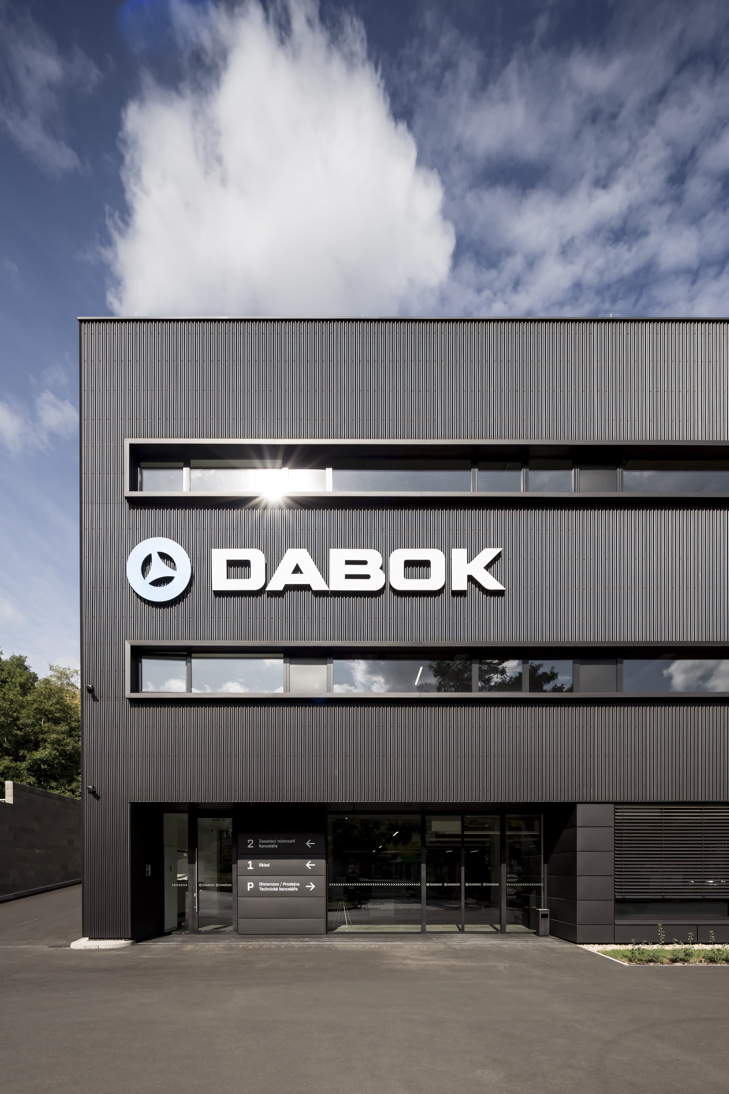 Detail nároží fasády z černého vlnitého plechu s velkým logem DABOK, pod ním prosklený vstup do showroomu